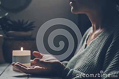 Woman at home in zen meditation activity and candlelight in background. One female people with hands up pray or meditate alone in Stock Photo