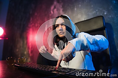 Woman in the hood sitting and working at laptop as hacker. Running malware program on computer in the internet with Stock Photo