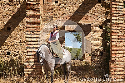 Woman horsewoman, young and beautiful, standing, riding her horse, in the field next to a ruined building. Concept horse riding, Stock Photo