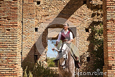 Woman horsewoman, young and beautiful, standing, riding her horse, in the field next to a ruined building. Concept horse riding, Stock Photo