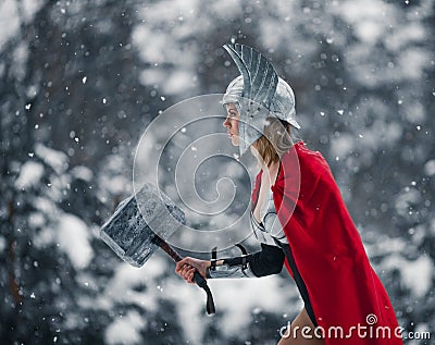 Woman in image of Germanic-Scandinavian God of thunder and storm goes with hammer in her hand. Cosplay. Stock Photo