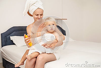 Woman and infant baby in white towels after bathing apply sunscreen or after sun lotion or cream. Children skin care in a hotel or Stock Photo