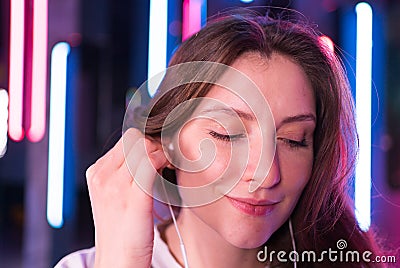 A woman inserts headphones into her ears and dances in the neon. Happy emotional beauty listens to music with headphones Stock Photo