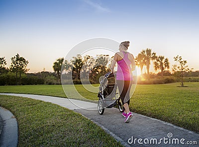 Woman jogging and exercising outdoors pushing her baby in a stroller Stock Photo