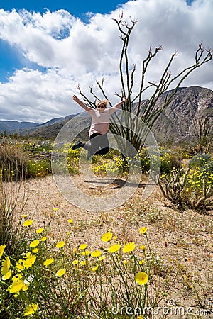 Woman jumps for joy next to an Ocotillo plant cactus. Wildflowers in photo Stock Photo