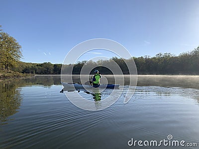 Woman kayaking on still waters with fog and sun glare Stock Photo
