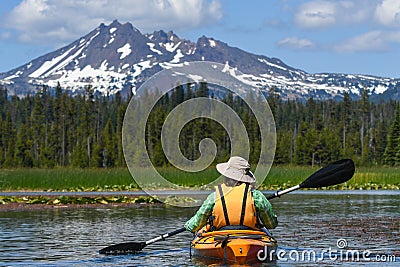 Woman kayaking toward snowy mountain peak Stock Photo