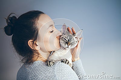 Woman is kissing and cuddling her sweet and cute looking Devon Rex cat. Kitten feels happy to be with its owner. Kitty sits in Stock Photo