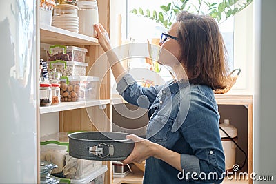 Woman in kitchen pantry. Storage wooden stand with kitchenware, products necessary to cook Stock Photo