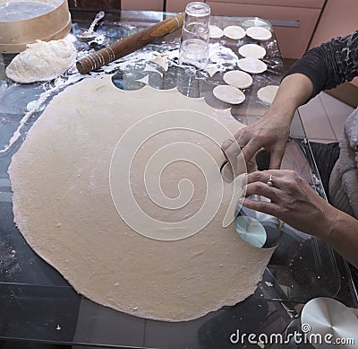 The woman kneaded the dough and made the blanks. Dough, rolling pin, sieve, spoon, glass on the table. Stock Photo