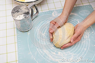 A woman kneads the dough with her hands, the hands of a baker, a silicone mat, a sieve, handmade baking. View from above Stock Photo