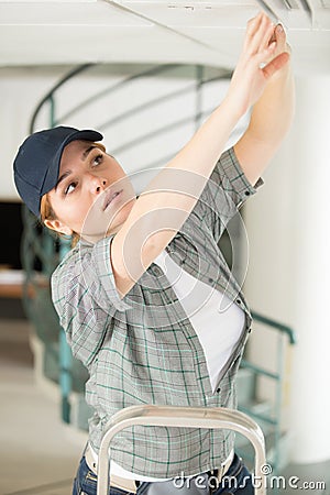 Woman on ladder fitting light bulb in new house Stock Photo