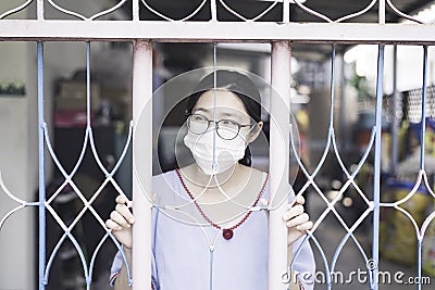 Woman / Lady ware surgical face mask and home quarantine herself or social distancing in house by holding door ar gate grill and Stock Photo