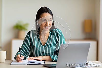 Woman At Laptop Taking Notes Learning Wearing Earbuds In Office Stock Photo