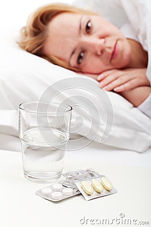 Woman laying sick with pills and glass of water Stock Photo