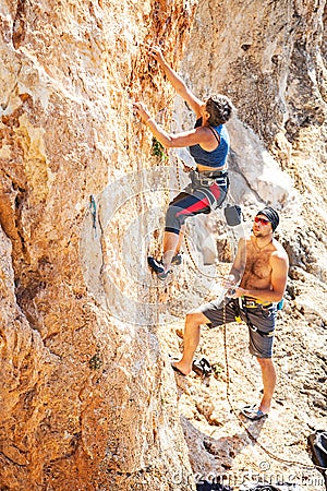 Woman lead climbing on natural cliff, guy belayer watching her Stock Photo