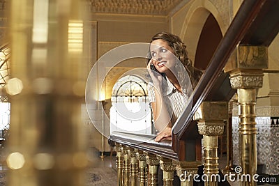 Portrait of young attractive woman talking on smartphone while leaning on railing Stock Photo