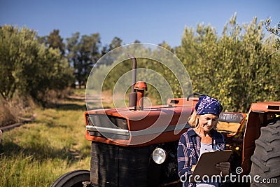 Woman leaning on tractor while writing on clipboard Stock Photo