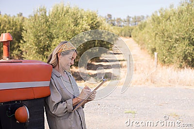 Woman leaning on tractor while writing on clipboard Stock Photo