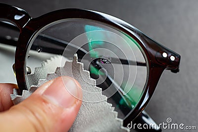 Woman left hand cleaning shortsighted or nearsighted eyeglasses by microfibre cleaning cloths, On black background, Close up Stock Photo