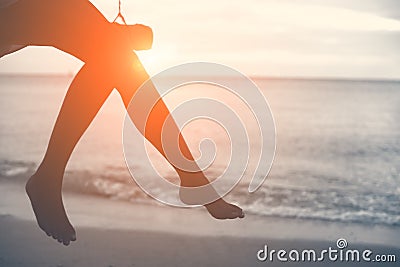 Woman legs at beach on wooden swing with sunset. Single woman co Stock Photo