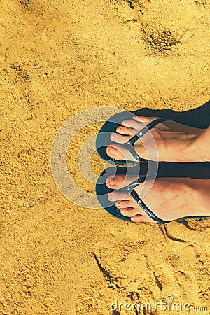 Woman legs in slippers on yellow sand background. Blue flip flops on beach. Copy space, top view. Holiday and travel Stock Photo