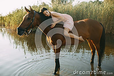 Woman lies astride a horse at river Stock Photo