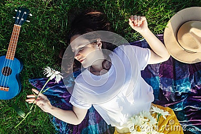 Woman lies on a purple blanket. On her body is a bouquet of daisies. Meditative state in a public park. On background of the Stock Photo