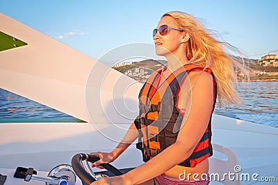 Woman in life-jacket stands at helm of motorboat Stock Photo