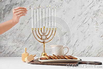 Woman lighting candles on menorah for Hanukkah on table with dreidels and potato pancakes Stock Photo