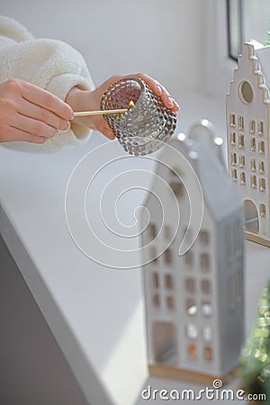 Woman lightning up candle near windowsill with house shaped lanterns indoors, closeup Stock Photo