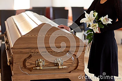 Woman with lily flowers and coffin at funeral Stock Photo