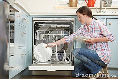 Woman Loading Dishwasher In Kitchen Stock Photo