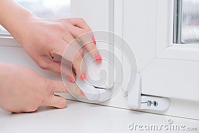 Woman locks a child safety lock on a window frame an apartment on a high floor Stock Photo