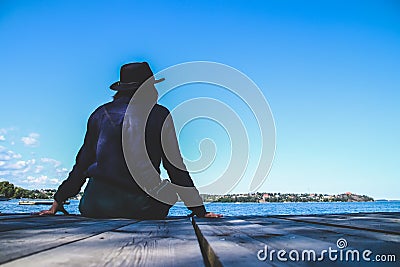 A woman lonely sitting on the wooden pier at the sea with blue sky. Stock Photo