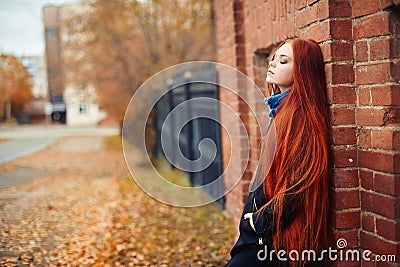 Woman with long red hair walks in autumn on the street. Mysterious dreamy look and the image of the girl. Redhead woman walking Stock Photo