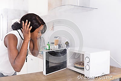 Woman Looking At Burnt Pizza In Microwave Oven Stock Photo