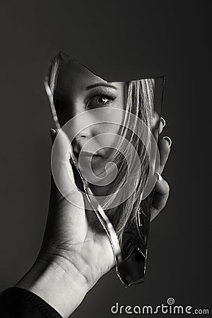 Woman looking at her face in a shard of broken mirror artistic c Stock Photo