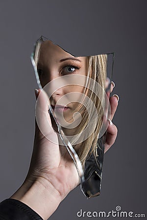 Woman looking at her face in shard of broken mirror Stock Photo