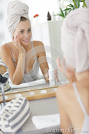 woman looking in mirror applying beauty product around eyes Stock Photo