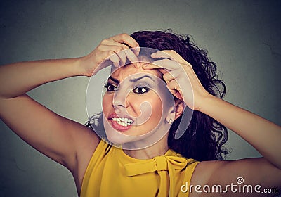 Woman looking in a mirror squeezing acne or blackhead on her face Stock Photo