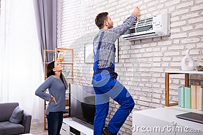 Woman Looking At Technician Repairing Air Conditioner Stock Photo