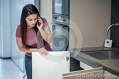 Woman looking under kitchen sink talking on smartphone Stock Photo