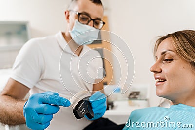 Woman looking at veneers or implants teeth color matching samples in doctor hands. Dentistry. Dentist demonstrate teeth Stock Photo
