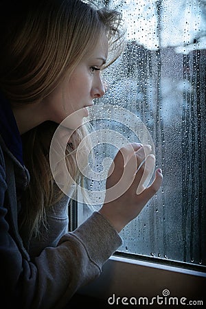 Woman looking through window with raindrops Stock Photo