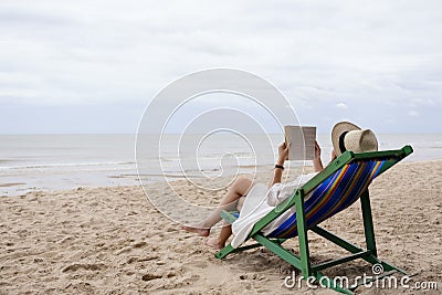 A woman lying down and reading book on the beach chair with feeling relaxed Stock Photo