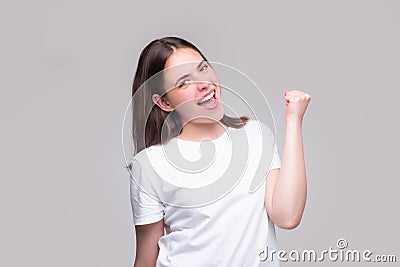 Woman make winner gesture. Portrait of attractive crazy girl breakthrough lucky isolated on gray background. Stock Photo