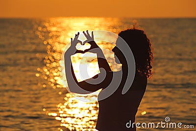 Woman makes heart by hands at sunset Stock Photo