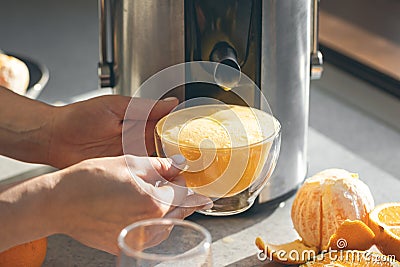 A woman makes orange juice at home in the kitchen with an electric juicer. Stock Photo