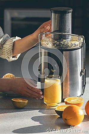 A woman makes orange juice at home in the kitchen with an electric juicer. Stock Photo